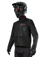 Alpinestars Pro-Dura Jacket, veste de moto tout-terrain, noire avec logos rouges et gris, dotée de poches avant zippées et d'un col montant, portée avec un casque de motocross noir et des gants pour l'enduro