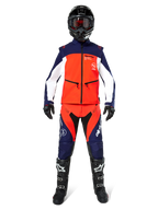 Pilote de motocross portant un équipement tout-terrain complet, veste Softshell Lite-Dura Alpinestars en bleu marine, orange vif et blanc, pantalon assorti marine et orange, casque noir avec lunettes, bottes noires et blanches, gants noirs, tenue coordonnée pour la course d'enduro.