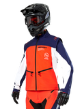 Veste Softshell Alpinestars Lite-Dura en bleu marine, orange vif et blanc, équipement de motocross, portée avec un casque et des lunettes noirs, des gants de protection et un pantalon de course assorti