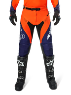 Pantalon Alpinestars Pro-Dura, pantalon de motocross et d'enduro, bleu marine, orange vif et blanc, avec empiècements noirs et logos blancs, porté avec des bottes et des gants tout-terrain noirs, équipement de protection professionnel pour le trail et le tout-terrain
