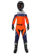 Pilote de motocross portant le pantalon Alpinestars Pro-Dura en Navy Hot Orange White, avec un maillot à manches longues assorti, un casque noir avec lunettes, des gants noirs et des bottes de motocross noires, équipement complet de course tout-terrain.