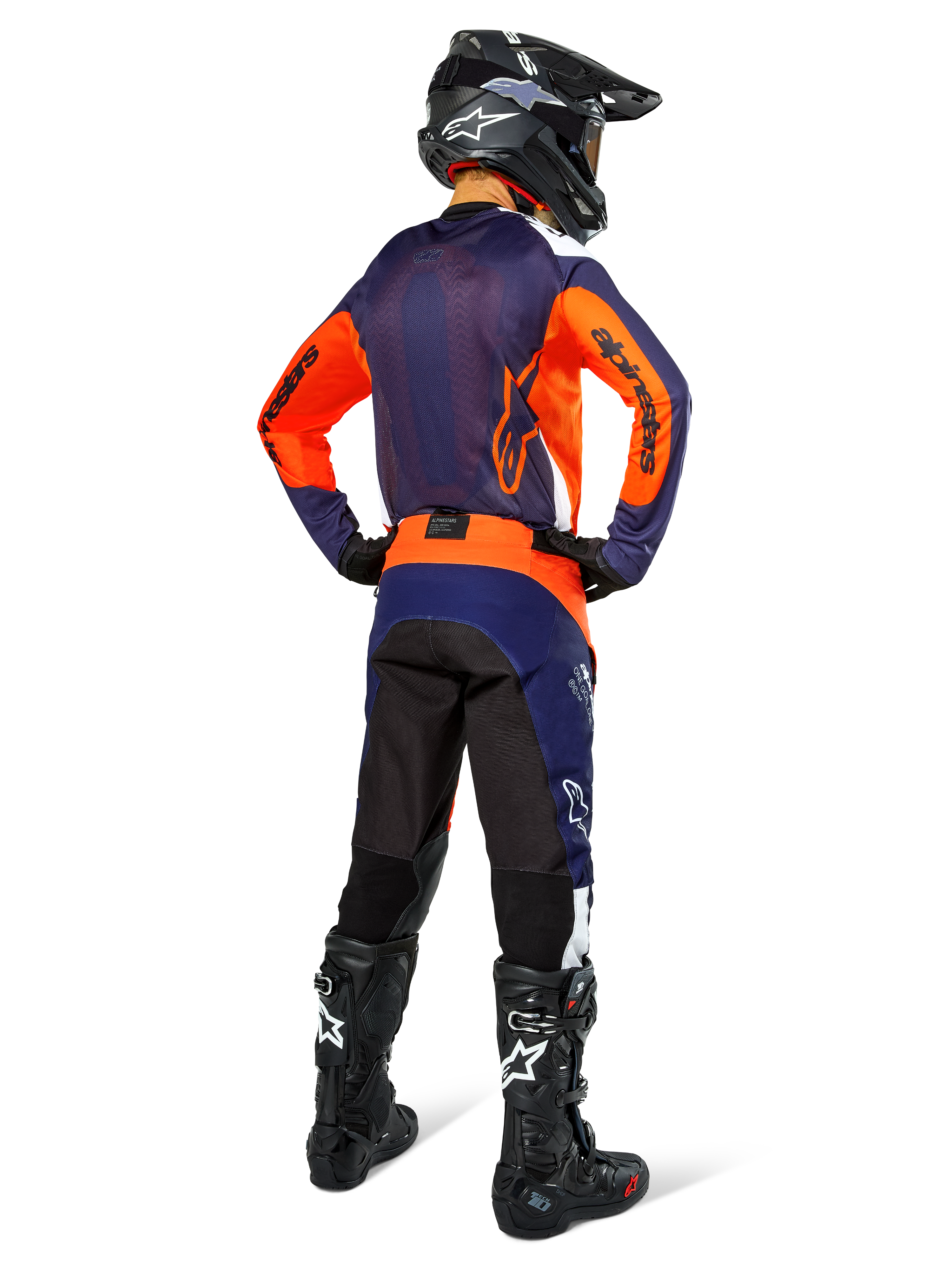 Pilote de motocross de dos portant une tenue de course complète Alpinestars, maillot bleu navy et orange, pantalon Pro-Dura en Navy Hot Orange White, casque noir et bottes noires, ensemble professionnel de course tout-terrain