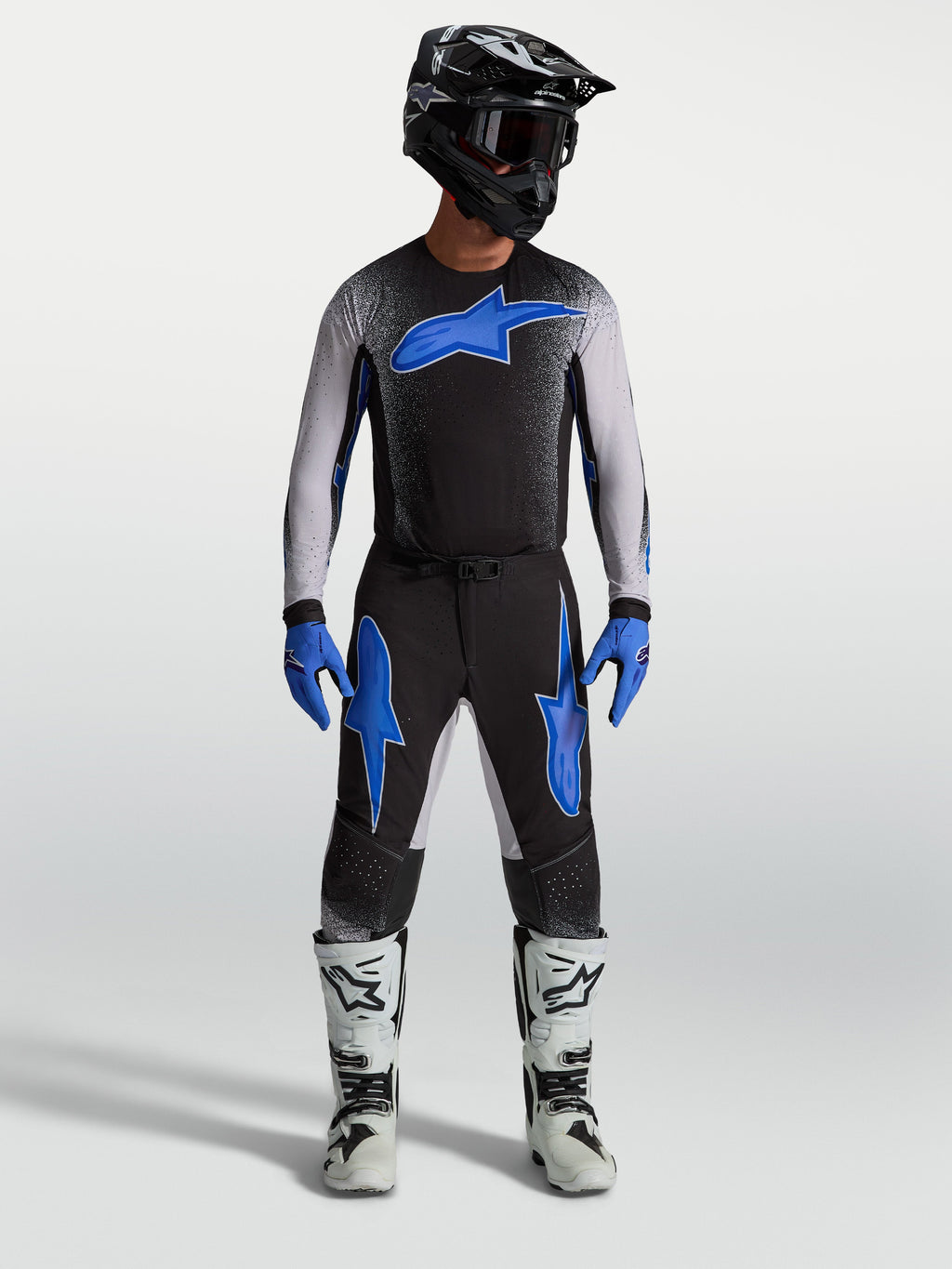 Pantalons Alpinestars Supertech Hiten AFD, équipement de motocross noirs et bleus, portés par un mannequin avec un maillot assorti et des bottes blanches, style performance tout-terrain.