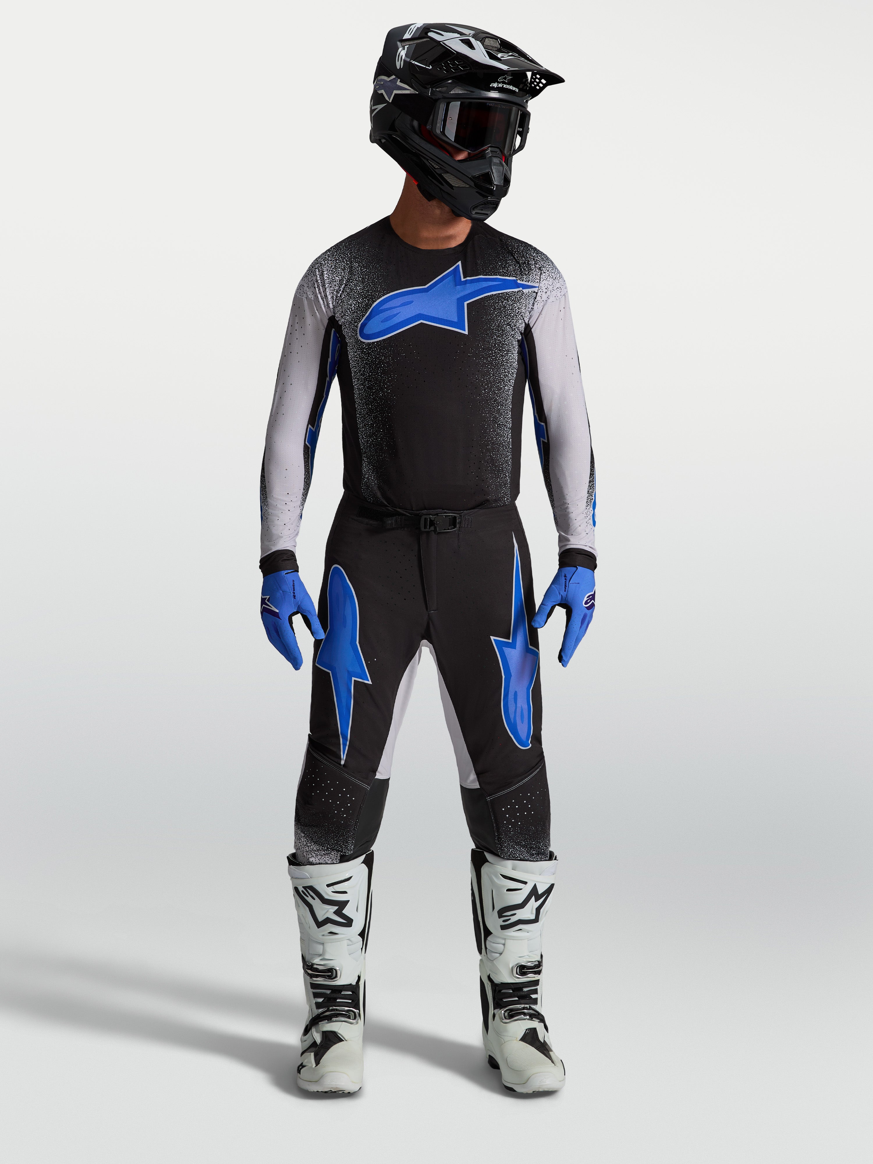 Pantalons Alpinestars Supertech Hiten AFD, équipement de motocross noirs et bleus, portés par un mannequin avec un maillot assorti et des bottes blanches, style performance tout-terrain.