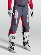 Alpinestars Supertech Hiten AFD, pantalon de motocross gris et rouge fluo avec graphismes d'étoiles blanches et boucle magnétique, porté avec des bottes blanches