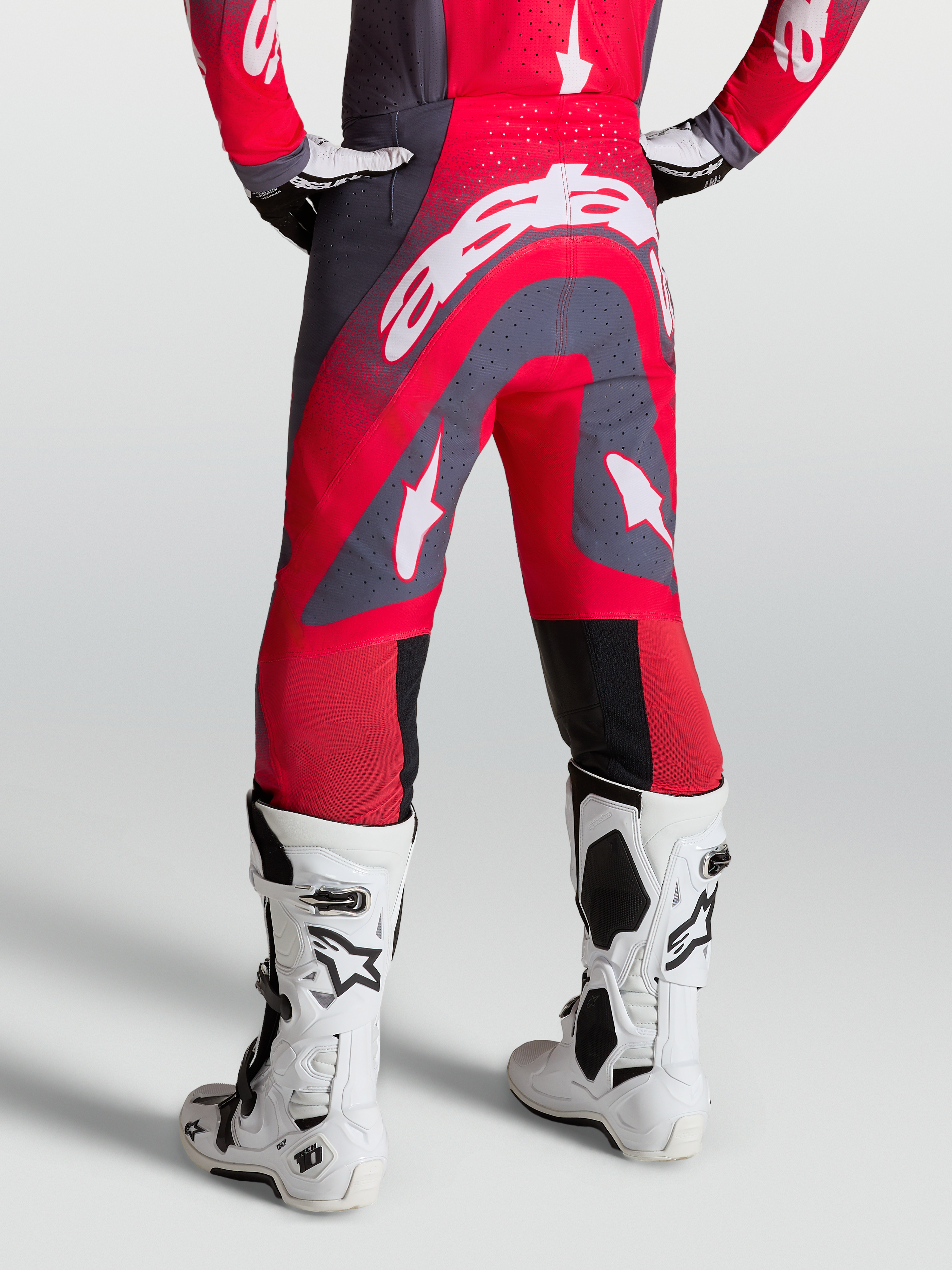 Alpinestars Supertech Hiten AFD, pantalon de motocross rouge et gris, vue arrière sur mannequin avec bottes de course blanches, coupe athlétique pro racing.