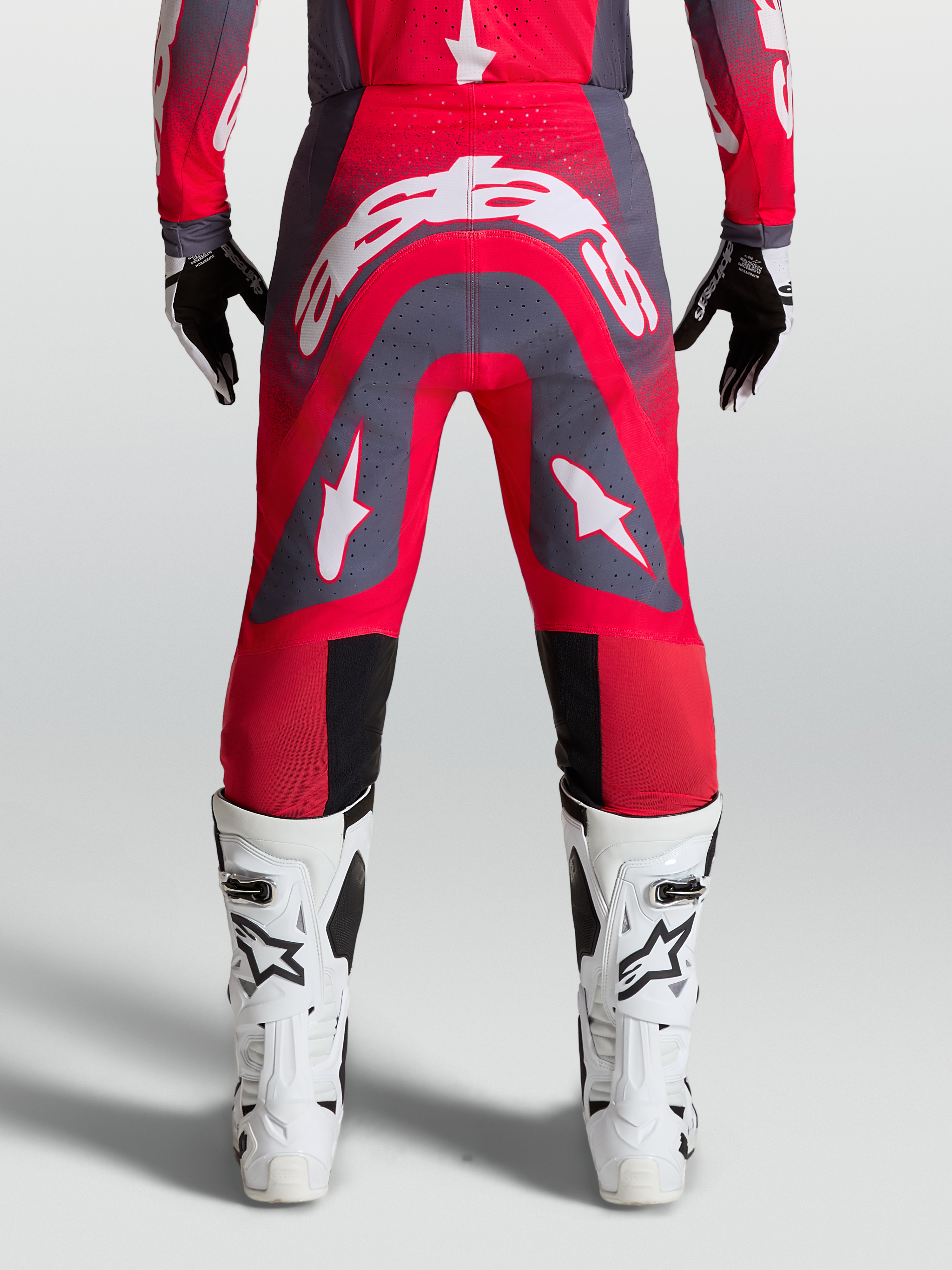 Alpinestars Supertech Hiten AFD, pantalon de motocross professionnel pour homme, rouge fluo et gris avec logos blancs, vue de dos montrant la coupe athlétique et les zones perforées pour la ventilation.