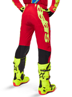 Alpinestars Supertech Maker Pants 2025, pantalon de motocross, rouge vif et jaune fluo, vue arrière, avec marquage jaune audacieux, panneaux noirs derrière les genoux, porté avec des bottes jaune fluo assorties, conçu pour des performances tout-terrain de niveau professionnel