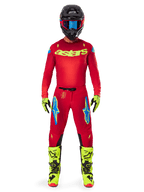 Pilote de motocross en tenue de course complète, maillot rouge avec logo astars jaune fluo, pantalon Alpinestars 2025 Supertech Maker rouge vif et jaune fluo, logos bleus sur les cuisses, gants et bottes jaune fluo, casque noir avec lunettes bleues, équipement de motocross professionnel coordonné
