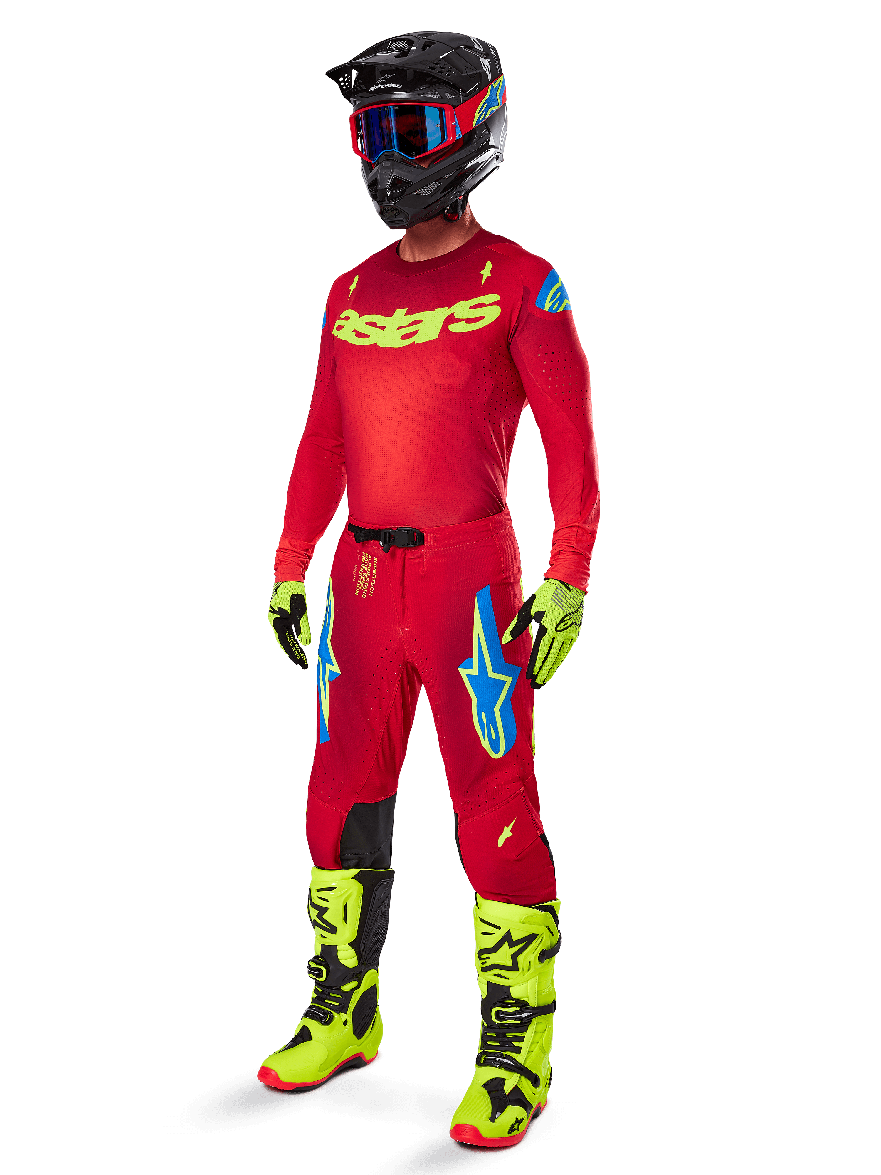 Pilote de motocross portant une tenue de course Alpinestars complète, pantalon Supertech Maker 2025 rouge vif et jaune fluo, maillot rouge assorti avec logo jaune fluo, bottes jaune fluo et noires, casque noir avec lunettes bleues, tenue professionnelle pour la course tout-terrain