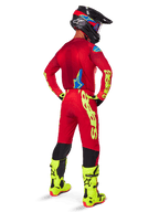 Pantalon Supertech Maker 2025 Alpinestars, pantalon de motocross, rouge vif et jaune fluo, vu de dos sur un pilote portant un maillot rouge assorti, des bottes jaune fluorescent et un casque noir, avec un grand logo Alpinestars jaune sur la jambe.