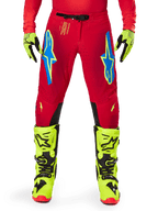 Alpinestars Supertech Maker Pants 2025, pantalon de motocross, rouge vif et jaune fluo, porté avec des gants et des bottes jaune fluo assortis, avec logos Astars bleus et jaune fluo, panneaux intérieurs aux genoux noirs et design athlétique pour la course tout-terrain
