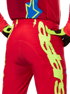 Alpinestars 2025 Supertech Maker Pants, pantalon de motocross, rouge vif et jaune fluo, vue arrière présentant de larges graphismes jaunes sur les jambes et des gants assortis jaune fluo et noir, équipement de course professionnel tout-terrain