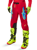 Pantalon Alpinestars Supertech Maker 2025, pantalon de course de motocross, rouge vif avec logos étoiles bleus et jaunes, empiècements noirs aux genoux, ventilations perforées, coordonné avec des bottes et des gants jaune fluo