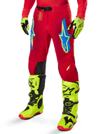 Pantalon Alpinestars Supertech Maker 2025, pantalon de course de motocross, rouge vif avec logos étoiles bleus et jaunes, empiècements noirs aux genoux, ventilations perforées, coordonné avec des bottes et des gants jaune fluo