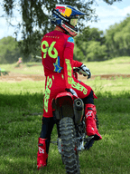 Pilote de motocross portant la tenue Alpinestars Supertech Maker 2025 en rouge vif et jaune fluo, assis sur une moto rouge, numéro 96 sur le maillot, bottes et casque rouges assortis, équipement de course professionnel pour performance tout-terrain