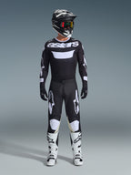 Ensemble d'équipement Alpinestars 2026 Racer Air Riway, tenue de motocross complète, noir et blanc, comprenant un maillot noir avec marquage « astars » blanc, un pantalon assorti avec empiècements blancs aux genoux, des bottes blanches avec boucles noires et un casque noir avec lunettes teintées rouge, équipement de course tout-terrain professionnel.