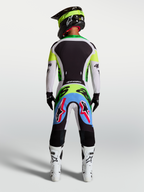 Pantalon Alpinestars Supertech Dyna, pantalon de motocross lilas et vert fluo, vue arrière d'un pilote en kit de course.