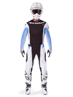 Pilote de motocross portant le pantalon Alpinestars Techstar Melt 2025, pantalon de motocross, noir et bleu, design multi-panneaux blanc et noir avec des accents bleus sur les hanches, porté avec un maillot blanc assorti, un casque blanc, des gants blancs et des bottes pour un équipement de course tout-terrain complet