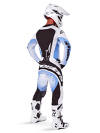 Pilote de motocross vu de dos portant le pantalon et le maillot Alpinestars 2025 Techstar Melt, design dégradé noir, bleu et blanc, casque blanc, bottes blanches et noires, tenue de course tout-terrain complète.