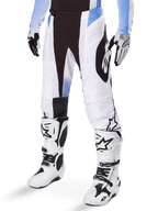 Alpinestars 2025 Techstar Melt Pants, pantalon de motocross, blanc et noir avec des accents bleus, avec perforations laser pour la ventilation et construction de genou Babel, porté avec des bottes et des gants de motocross blancs assortis, design de course tout-terrain athlétique