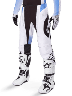 Alpinestars 2025 Techstar Melt Pants, pantalon de motocross, blanc et noir avec des accents bleus, avec perforations laser pour la ventilation et construction de genou Babel, porté avec des bottes et des gants de motocross blancs assortis, design de course tout-terrain athlétique