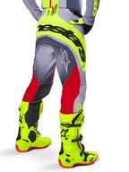 Alpinestars Techstar Melt Pants 2025, pantalon de motocross, rouge vif et gris avec des accents jaune fluo, vue arrière mettant en valeur le large logo noir sur l'assise, porté avec des bottes jaune fluo assorties et un maillot gris, coupe athlétique pour la compétition tout-terrain