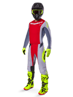 Pilote de motocross portant une tenue de course complète Alpinestars, maillot rouge et gris, pantalon Techstar Melt 2025 rouge vif et gris avec accents jaune fluo, bottes et gants jaune fluo, casque noir avec lunettes jaune fluo, tenue coordonnée pour la performance tout-terrain