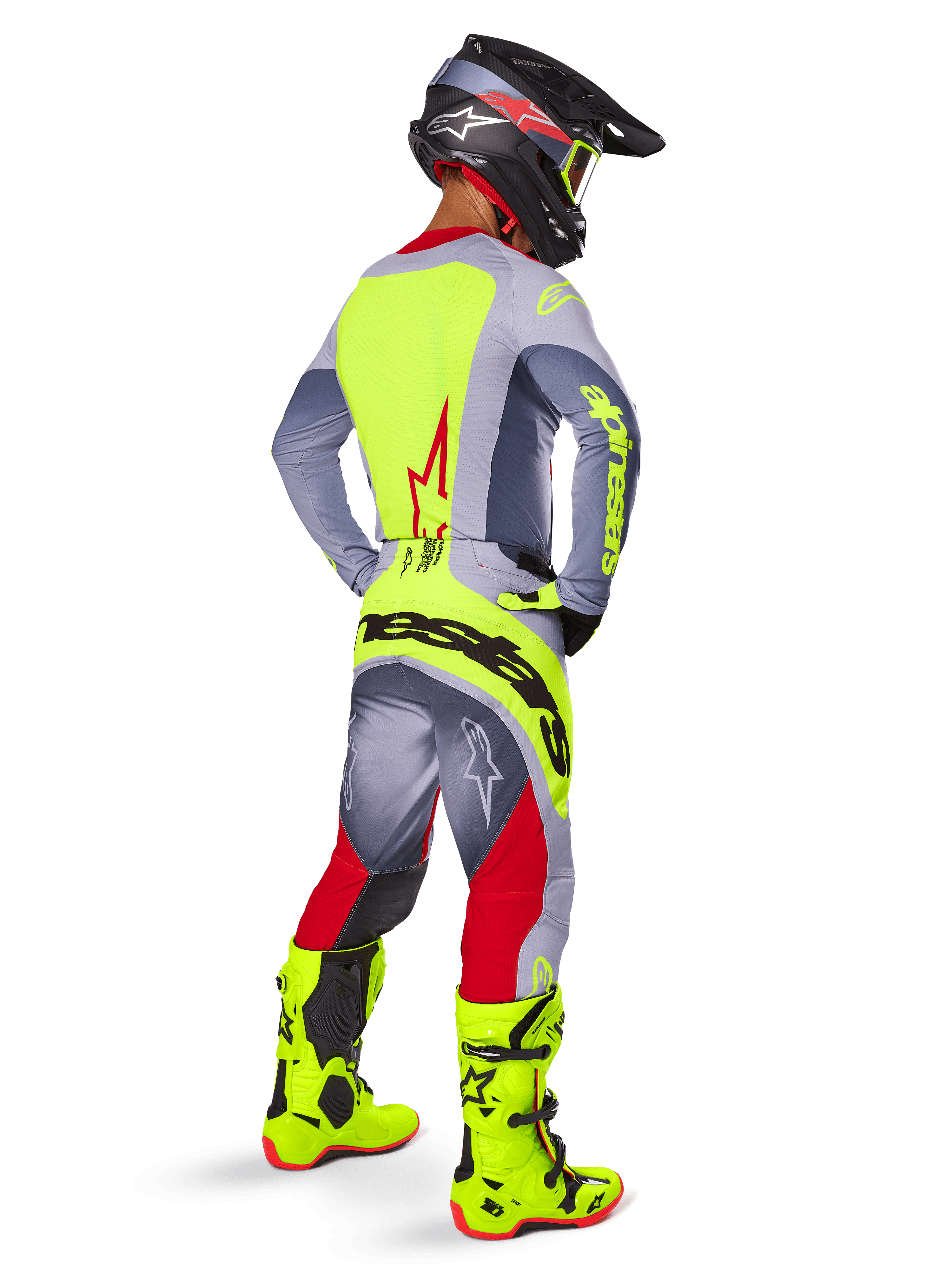 Pilote de motocross portant l'ensemble d'équipement Alpinestars Techstar Melt 2025, vu de dos. Maillot gris avec un panneau arrière jaune fluo et un logo étoile rouge, pantalon gris et rouge avec un marquage 'Alpinestars' jaune fluo imposant sur l'assise, bottes de motocross jaune fluo éclatant et casque assorti.