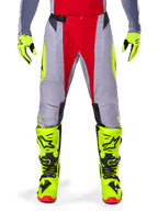 Alpinestars Techstar Melt Pants 2025, pantalon de motocross, rouge vif et gris avec des accents jaune fluo, porté avec des gants et des bottes jaune fluo assortis, doté d'une boucle de taille magnétique et de perforations laser pour la ventilation