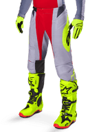 Alpinestars Techstar Melt Pants 2025, pantalon de motocross, rouge vif et gris avec un logo jaune fluo, porté avec des gants et des bottes jaune fluo assortis, coupe athlétique pour la course de motocross