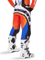 Pantalon Alpinestars Techstar Melt 2025, pantalon de motocross, orange et bleu, vu de dos, avec un grand logo blanc sur l'assise, porté avec un maillot orange assorti et des bottes Tech 10 blanches, équipement de course tout-terrain durable