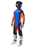 Ensemble d'équipement Alpinestars Techstar Melt 2025, pilote de motocross portant un maillot bleu à manches orange, un pantalon noir avec des accents bleus et orange, casque noir assorti avec lunettes bleues, et bottes de course blanches et noires