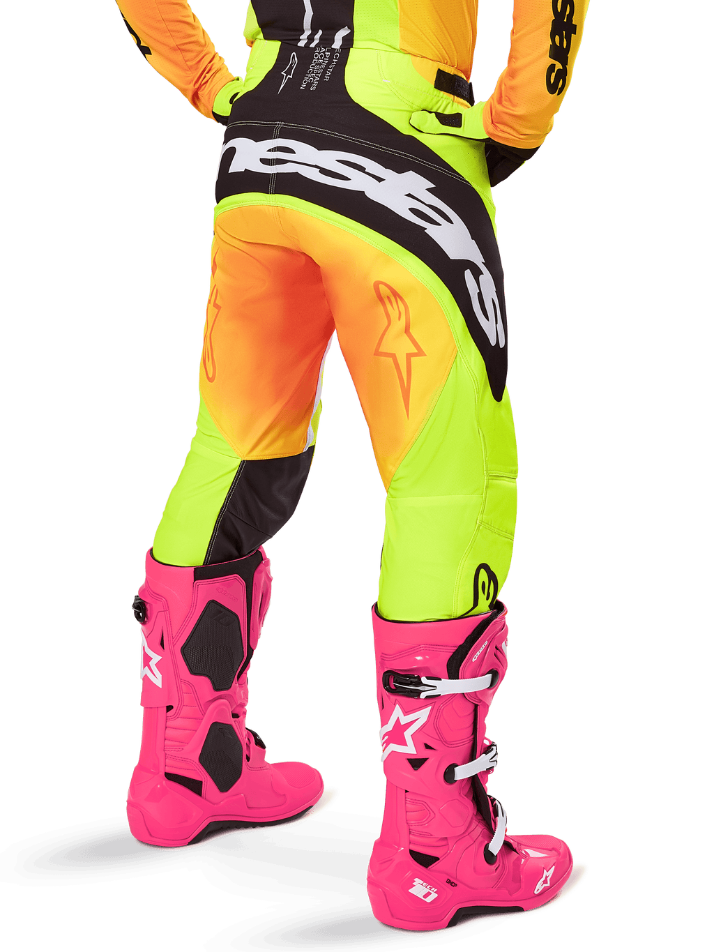 Vue arrière d'un pilote de motocross portant le pantalon Alpinestars Techstar Melt 2025, dégradé jaune et orange avec logo noir et blanc sur l'assise, associé à des bottes de motocross rose vif, équipement tout-terrain haute performance