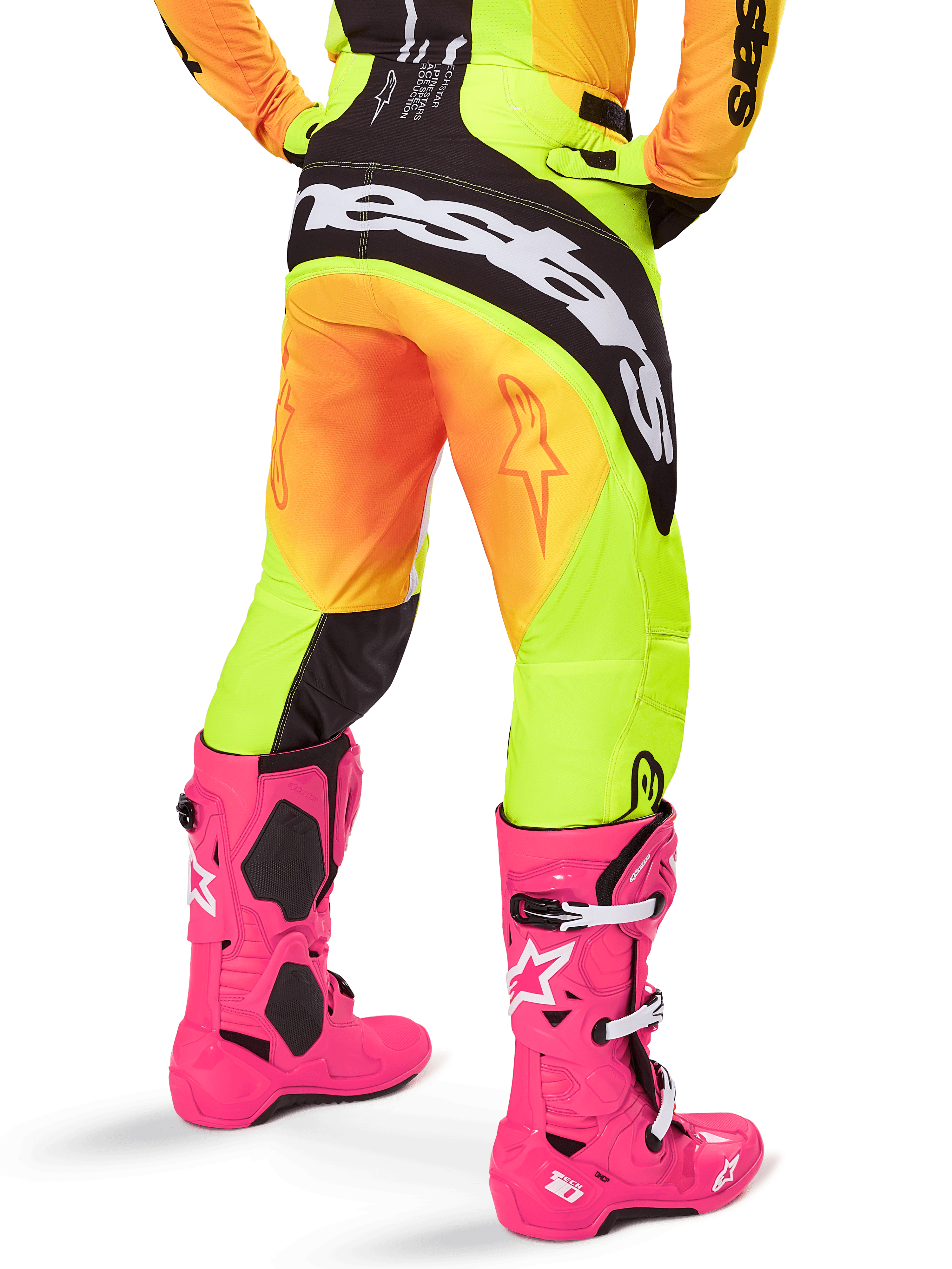 Vue arrière d'un pilote de motocross portant le pantalon Alpinestars Techstar Melt 2025, dégradé jaune et orange avec logo noir et blanc sur l'assise, associé à des bottes de motocross rose vif, équipement tout-terrain haute performance
