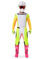 Pilote de motocross portant l'ensemble Alpinestars 2025 Techstar Melt, maillot blanc avec manches jaunes et orange, pantalon jaune fluo avec accents blancs et orange, casque blanc avec lunettes rouges, bottes rose vif et gants jaune fluo, tenue de course complète pour la compétition tout-terrain