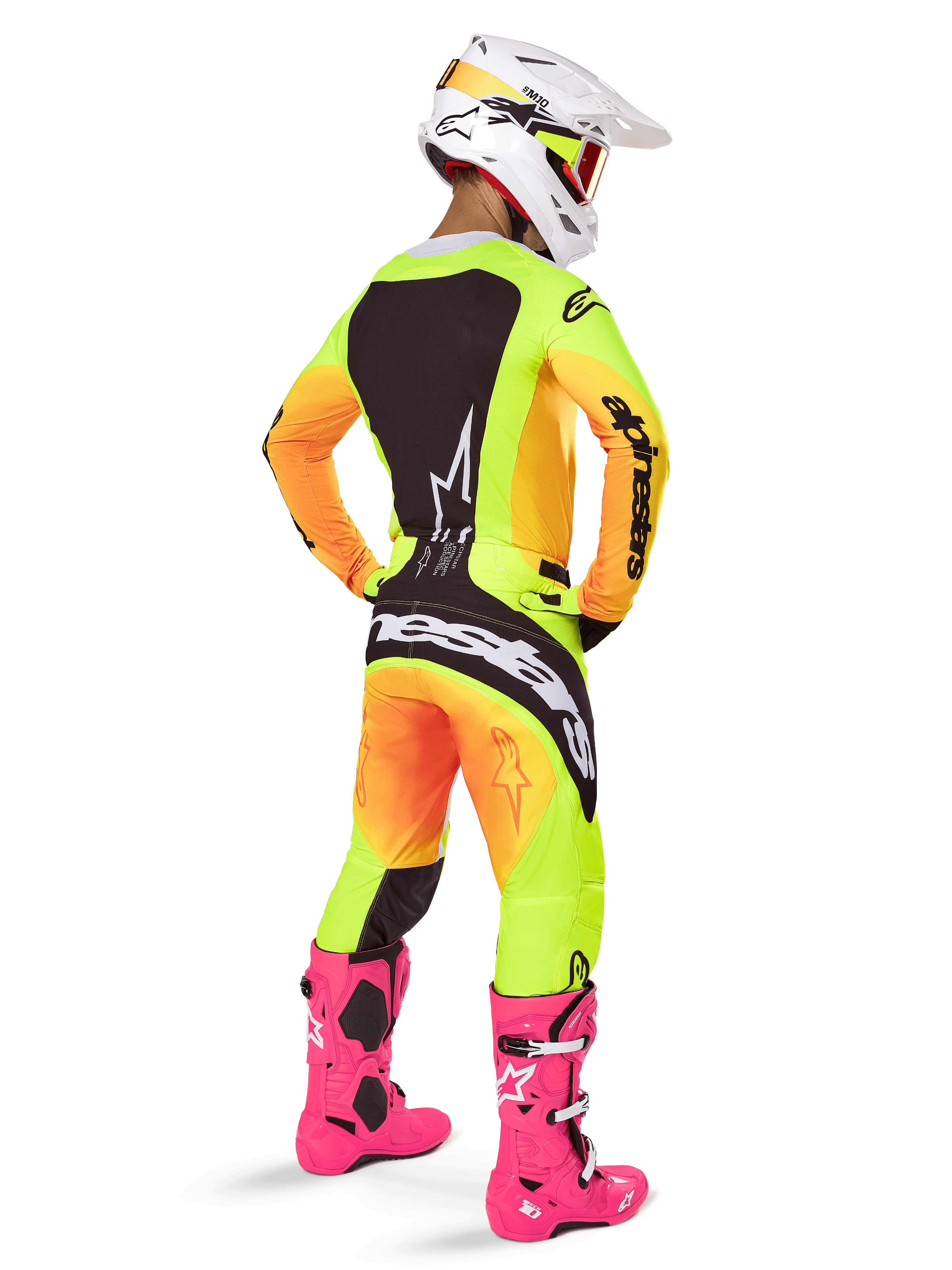 Pilote de motocross vu de dos portant l'ensemble Alpinestars Techstar Melt 2025, maillot et pantalon avec dégradé jaune et orange et empiècements noirs, casque blanc avec masque rouge, bottes rose vif, tenue de course coordonnée pour la performance tout-terrain