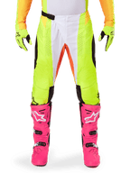 Alpinestars Pantalon Techstar Melt 2025, pantalon de motocross, jaune fluo et blanc avec accents orange, porté avec des gants jaunes assortis et des bottes de motocross rose vif, doté de panneaux de ventilation perforés et d'une boucle de taille magnétique, équipement de course haute performance
