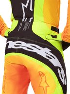 Pantalon Alpinestars Techstar Melt 2025, pantalon de motocross, vue arrière en gros plan, jaune fluo et orange avec empiècements noirs, grand logo Alpinestars blanc sur l'assise, équipement de performance pour le tout-terrain