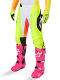 Alpinestars 2025 Techstar Melt Pants, pantalon de motocross, jaune fluo avec accents blancs et orange, motifs noirs sur les côtés, porté avec des bottes de motocross rose vif et des gants jaune fluo, doté de ventilations perforées, équipement de course tout-terrain durable
