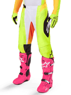 Alpinestars 2025 Techstar Melt Pants, pantalon de motocross, jaune fluo avec accents blancs et orange, motifs noirs sur les côtés, porté avec des bottes de motocross rose vif et des gants jaune fluo, doté de ventilations perforées, équipement de course tout-terrain durable