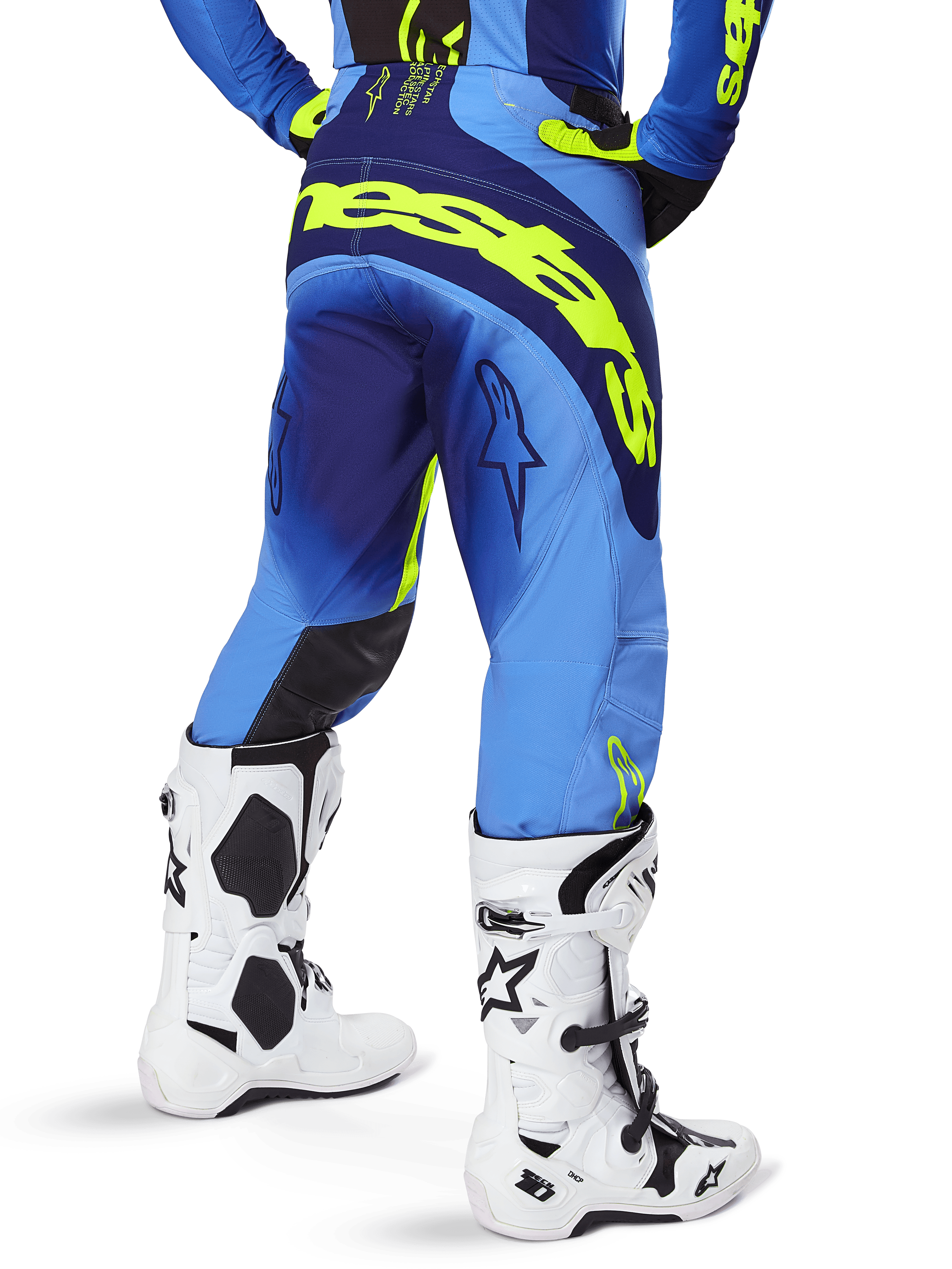 Alpinestars Techstar Melt Pants 2025, pantalon de motocross, jaune fluo et bleu, vue arrière avec un grand logo jaune sur l'assise et des détails bleu foncé, porté avec des bottes Alpinestars Tech 10 blanches et un maillot assorti