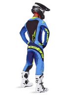 Alpinestars Techstar Melt Pants 2025, équipement de motocross, jaune fluo et bleu, vue arrière du pilote portant un maillot bleu assorti avec un large marquage jaune, des bottes blanches et noires et un casque noir, tenue de course coordonnée pour la performance tout-terrain