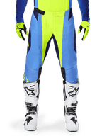 Alpinestars 2025 Techstar Melt Pants, pantalon de motocross, jaune fluo et bleu, porté avec des gants assortis et des bottes blanches, avec empiècements bleus et accents jaune fluo, design axé sur la performance pour la course tout-terrain