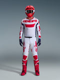 Pilote de motocross portant l'ensemble d'équipement Alpinestars 2026 Racer Riway, maillot blanc avec marquage « astars » rouge et panneaux latéraux bleus, pantalon blanc avec graphismes rouges, casque de course et bottes rouges, gants bleu marine, tenue de motocross complète et coordonnée
