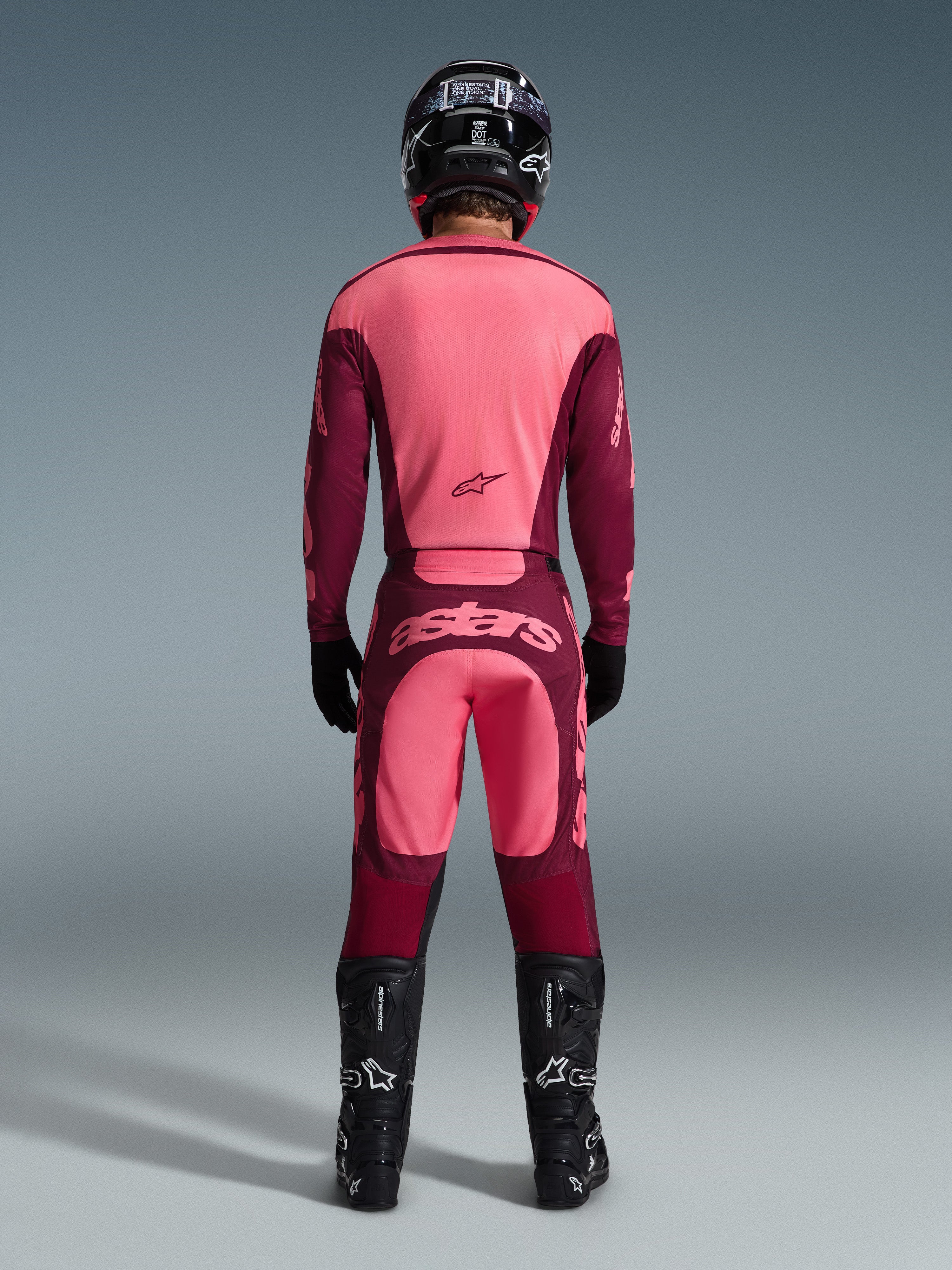 Motocross rider from the back wearing the Alpinestars 2026 Racer Riway Jersey and matching pants in Dark Red Coral, featuring black boots, a black helmet, and black gloves, coordinated high-performance gear for off-road racing