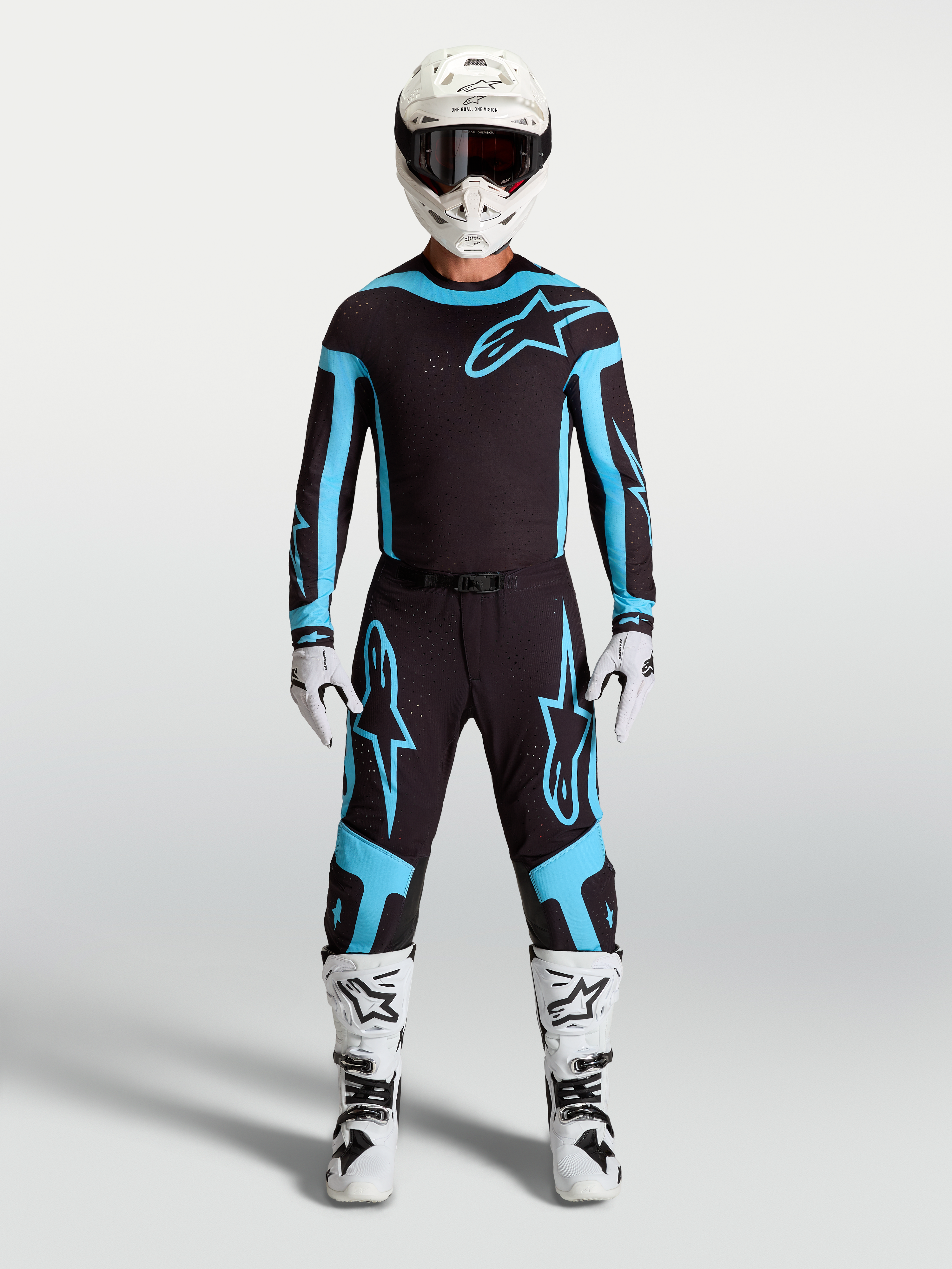 Pantalon Alpinestars Supertech Vesta, équipement de motocross pour homme, noir et turquoise, tissu extensible léger et coupe athlétique, porté par un mannequin avec bottes et casque
