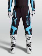 Alpinestars Pantalon Supertech Vesta, équipement motocross pro pour homme, noir et bleu turquoise avec larges graphismes d'étoiles et panneaux de genoux en cuir, porté par un pilote.