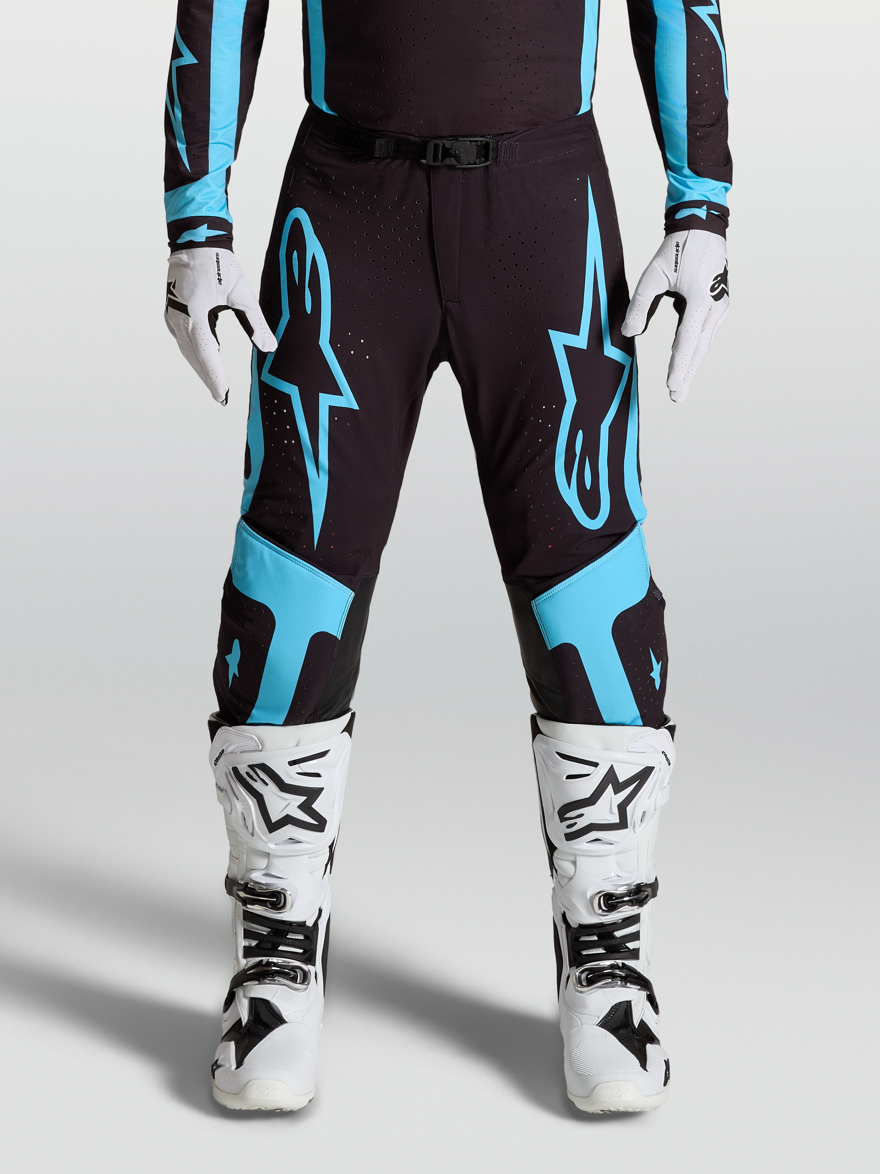 Alpinestars Pantalon Supertech Vesta, équipement motocross pro pour homme, noir et bleu turquoise avec larges graphismes d'étoiles et panneaux de genoux en cuir, porté par un pilote.