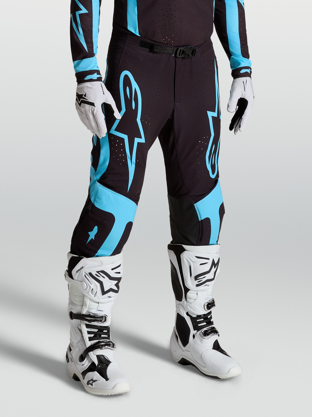 Alpinestars Pantalon Supertech Vesta, pantalon de motocross pour homme, noir et turquoise, tissu rip-stop extensible, panneaux en cuir de chèvre aux genoux, porté avec bottes blanches